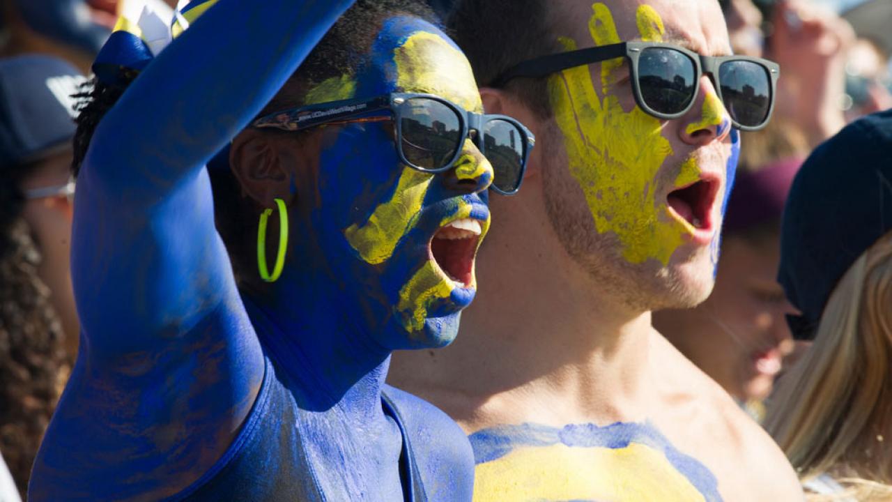 a male and female student painted in ֱ blue and gold cheer on the Aggies at the annual homecoming football game