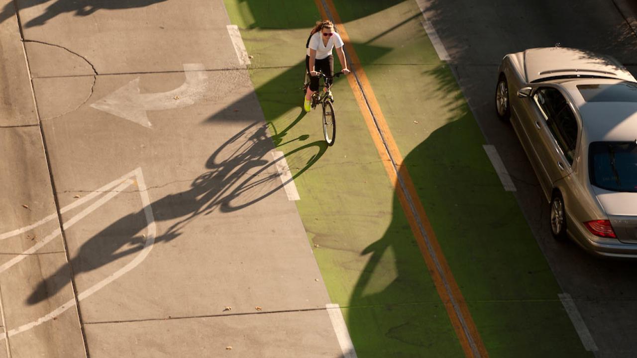 a female student rides her bike through a clearly marked green bike line next to a car on the ֱ campus