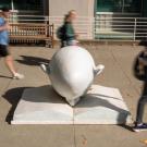Bookhead Egghead shot in front of library at ֱ with students, in blur, walking by