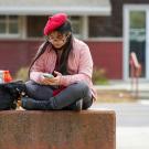 A student wearing a beret uses their smartphone outside of the ֱ Craft Center.