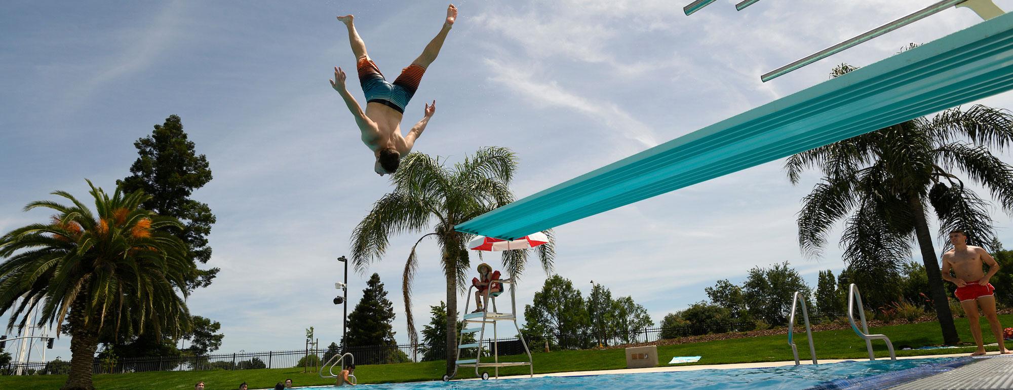 A student doing an acrobatic jump of of the diving board at the ֱ Recreation Pool